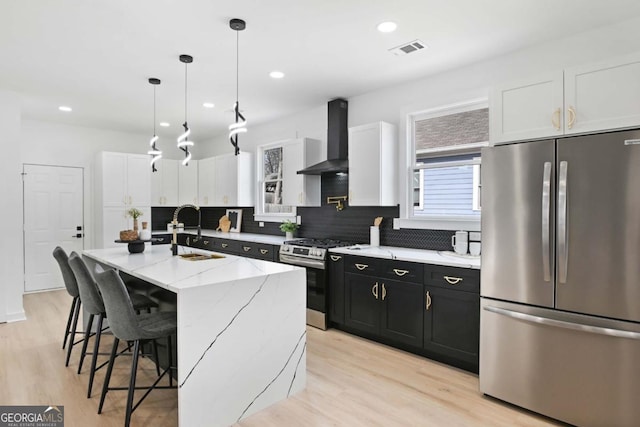 kitchen featuring appliances with stainless steel finishes, a kitchen island with sink, white cabinetry, and wall chimney exhaust hood