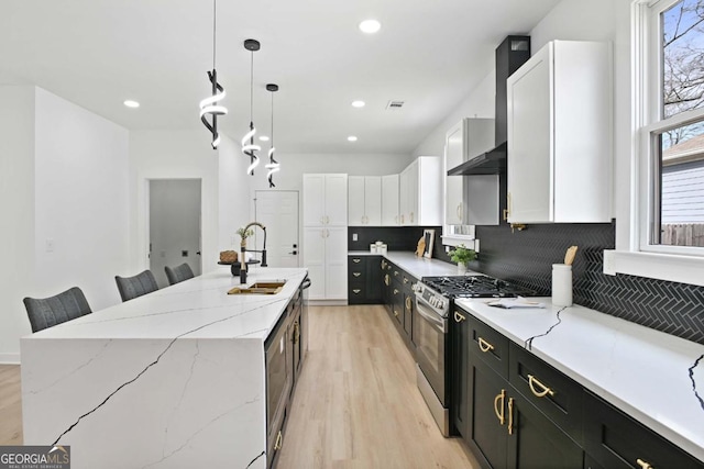 kitchen with dark cabinets, white cabinets, hanging light fixtures, gas range, and a center island with sink