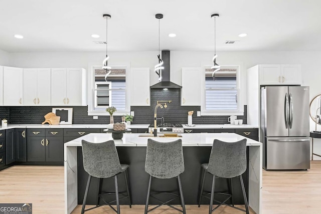 kitchen with freestanding refrigerator, hanging light fixtures, light countertops, wall chimney range hood, and white cabinetry