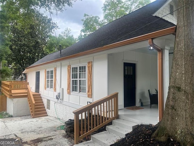 rear view of house featuring roof with shingles and stairs