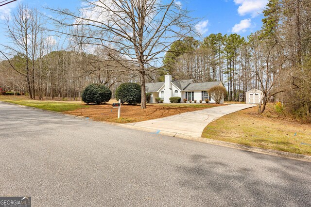 view of front of property with an outbuilding, a chimney, concrete driveway, and a front yard