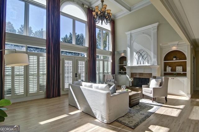 living area with built in shelves, coffered ceiling, light wood finished floors, a fireplace with raised hearth, and a towering ceiling