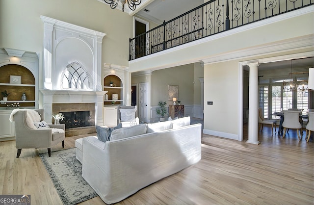 living room featuring built in shelves, a notable chandelier, wood finished floors, a fireplace, and decorative columns