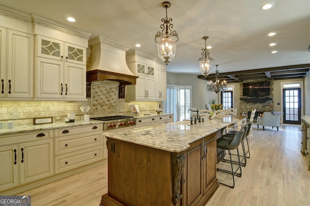 kitchen featuring premium range hood, a sink, light wood-style floors, stainless steel gas stovetop, and light stone countertops