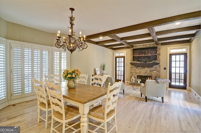 dining space with light wood-type flooring, beamed ceiling, a notable chandelier, a fireplace, and baseboards