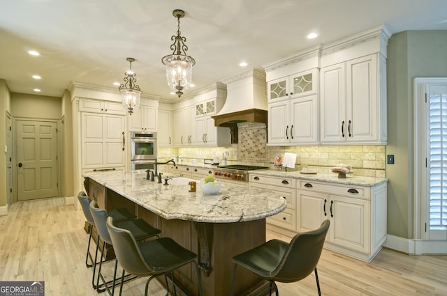 kitchen featuring custom exhaust hood, light wood finished floors, stainless steel appliances, and a kitchen breakfast bar