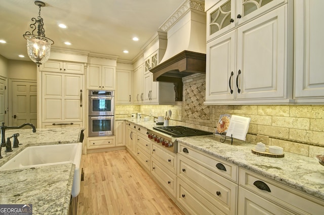 kitchen featuring light wood finished floors, a sink, decorative backsplash, appliances with stainless steel finishes, and pendant lighting