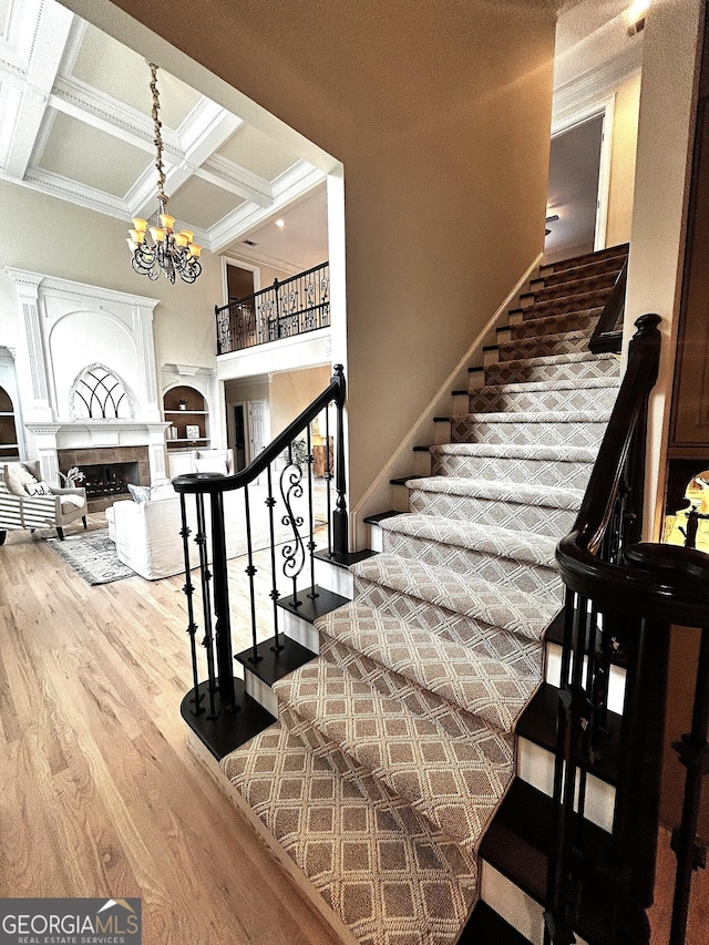 stairs with wood finished floors, coffered ceiling, an inviting chandelier, beam ceiling, and a fireplace