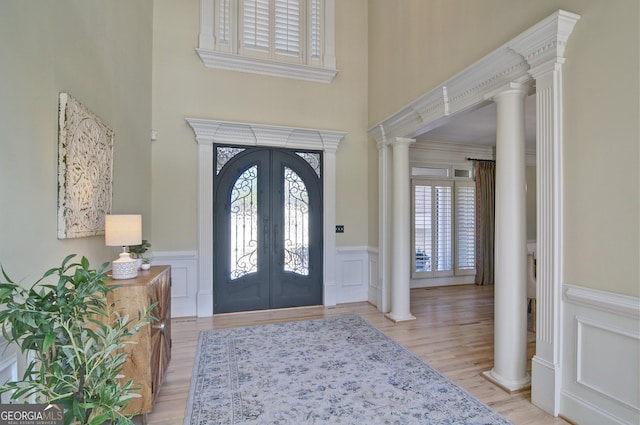 foyer featuring french doors, wood finished floors, wainscoting, and ornate columns