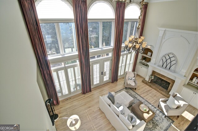 living area featuring visible vents, a tiled fireplace, french doors, light wood-style floors, and a chandelier