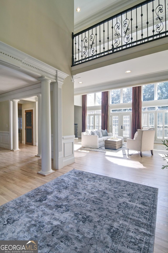 living area with wood finished floors, a towering ceiling, a healthy amount of sunlight, and ornate columns