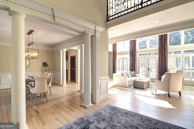 interior space featuring an inviting chandelier, wainscoting, light wood finished floors, crown molding, and ornate columns