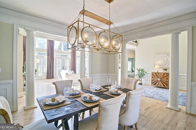 dining space featuring light wood-type flooring, decorative columns, crown molding, and a decorative wall