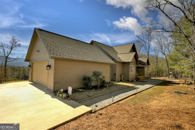 view of side of home with a shingled roof and a detached garage