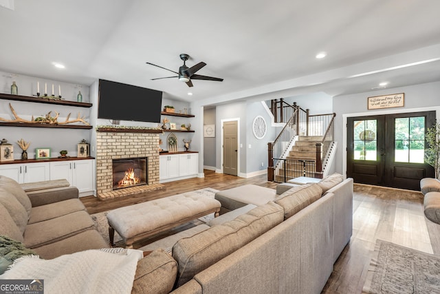 living area featuring french doors, stairway, a brick fireplace, and light wood-style flooring