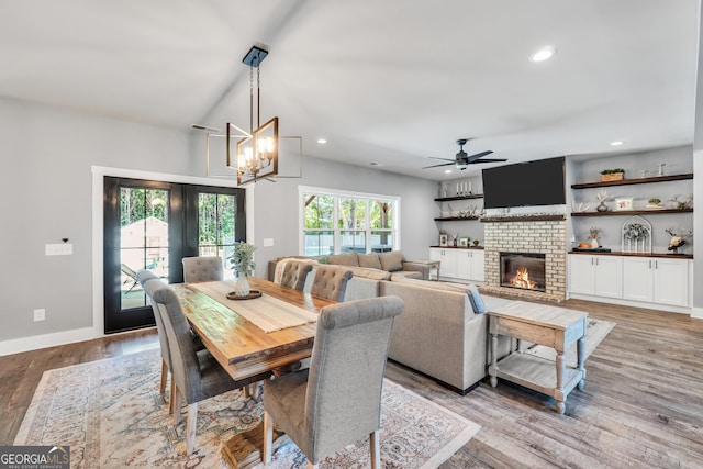 dining space with recessed lighting, baseboards, light wood-style floors, a fireplace, and ceiling fan with notable chandelier