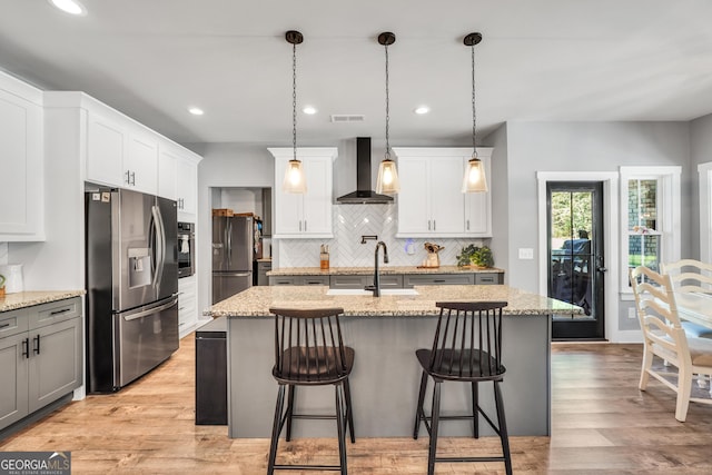 kitchen with visible vents, an island with sink, appliances with stainless steel finishes, decorative light fixtures, and wall chimney range hood