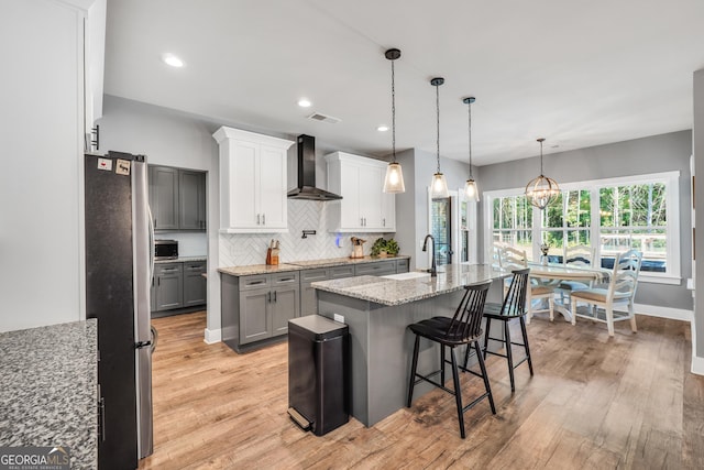 kitchen featuring wall chimney exhaust hood, visible vents, freestanding refrigerator, an island with sink, and a kitchen breakfast bar