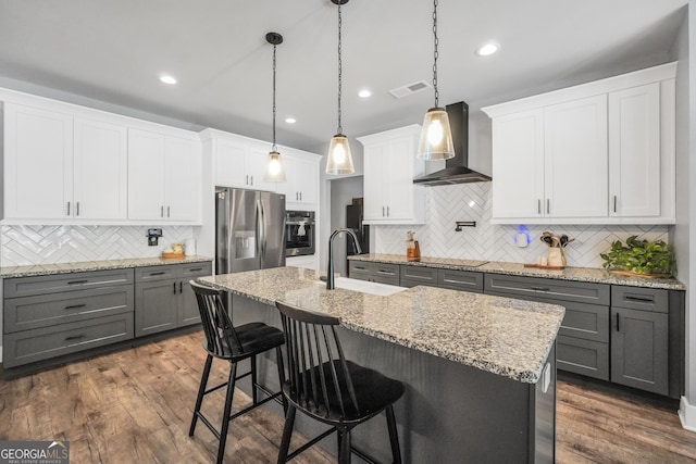 kitchen with wall chimney range hood, a kitchen island with sink, stainless steel appliances, and a sink