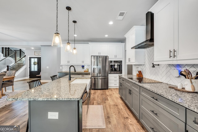 kitchen featuring decorative light fixtures, a center island with sink, visible vents, appliances with stainless steel finishes, and wall chimney range hood