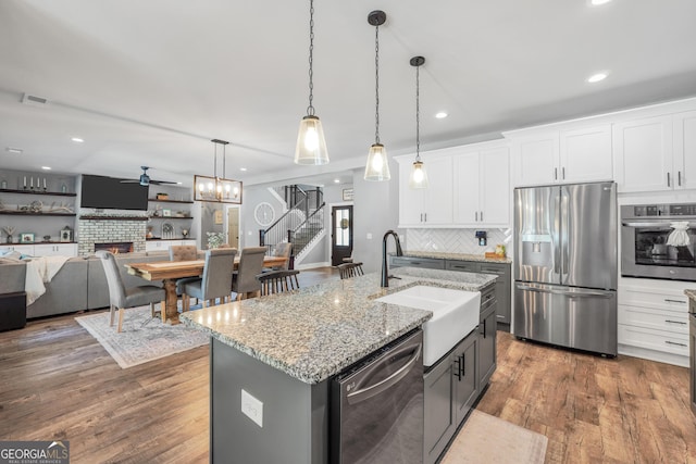 kitchen featuring decorative light fixtures, stainless steel appliances, open floor plan, white cabinets, and an island with sink