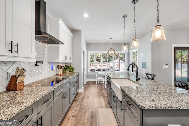 kitchen with pendant lighting, a kitchen island with sink, wall chimney range hood, and black electric cooktop