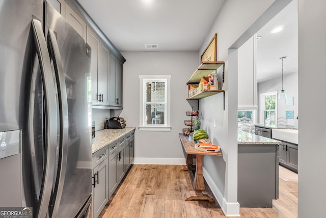 kitchen with light stone counters, pendant lighting, stainless steel appliances, gray cabinets, and light wood-style floors