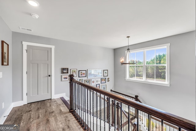 hallway with baseboards, visible vents, wood finished floors, and an upstairs landing