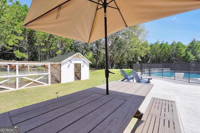 wooden terrace featuring an outbuilding, a patio, fence, a lawn, and a fenced in pool