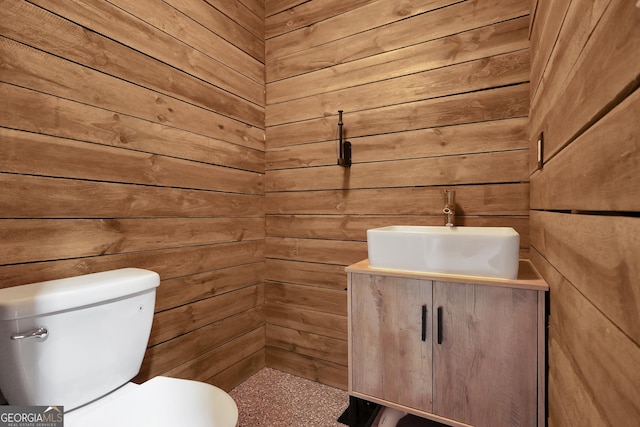 half bathroom featuring toilet, wood walls, and vanity