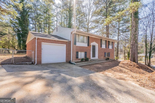 raised ranch with a garage, fence, concrete driveway, and brick siding