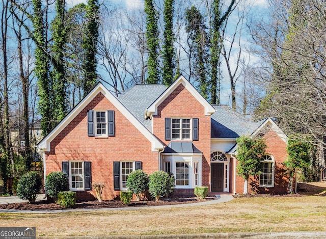 traditional-style house featuring a front lawn, roof with shingles, and brick siding