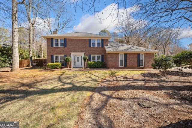 colonial inspired home with a front yard, brick siding, fence, and a chimney