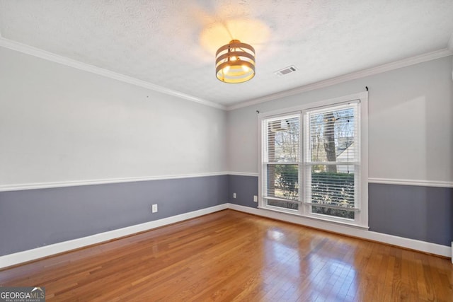 spare room featuring visible vents, hardwood / wood-style floors, ornamental molding, a textured ceiling, and baseboards