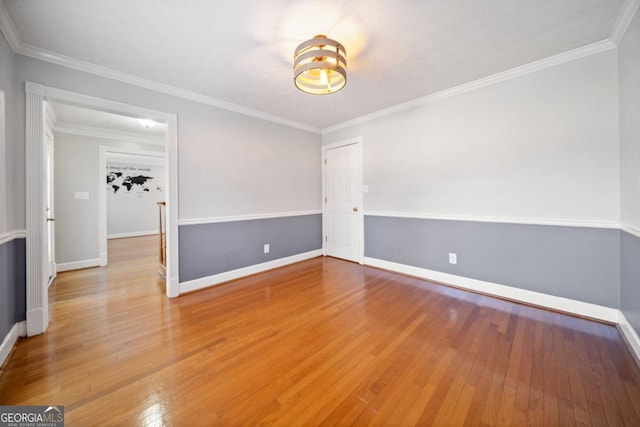 empty room with crown molding, wood-type flooring, and baseboards