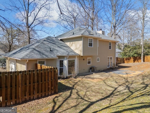 rear view of house with a shingled roof, a chimney, a patio area, and fence