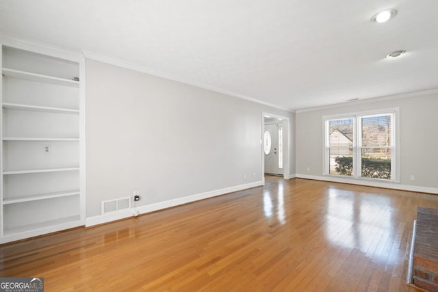 unfurnished living room featuring hardwood / wood-style flooring, visible vents, built in features, baseboards, and ornamental molding