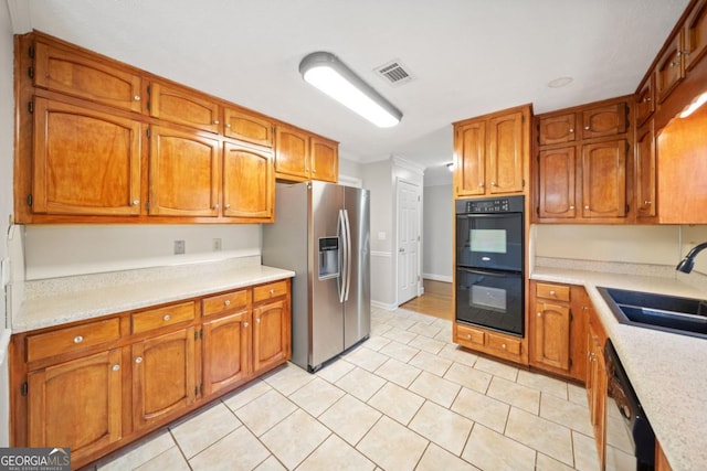 kitchen with brown cabinets, light countertops, visible vents, a sink, and black appliances