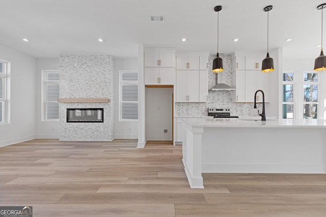 kitchen with white cabinetry, hanging light fixtures, electric range, and an island with sink