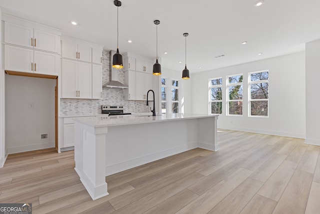 kitchen with white cabinets, wall chimney exhaust hood, a center island with sink, and stainless steel range with electric cooktop