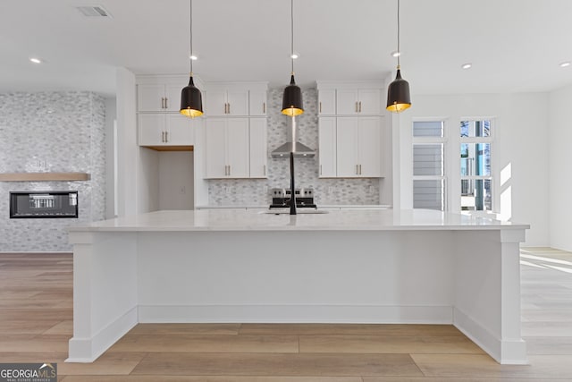 kitchen with pendant lighting, a glass covered fireplace, white cabinets, light wood-type flooring, and a large island with sink