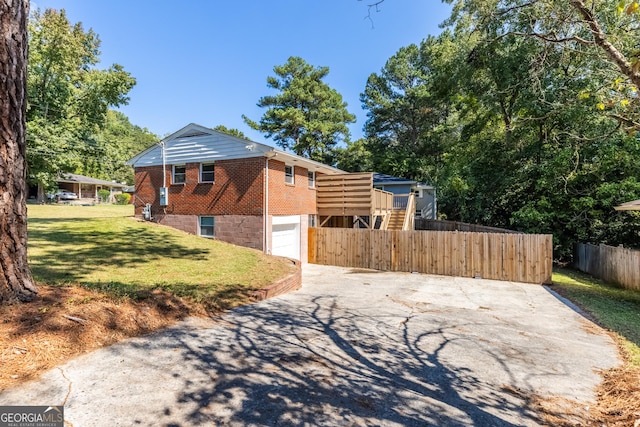 view of side of property with brick siding, a yard, an attached garage, fence, and driveway