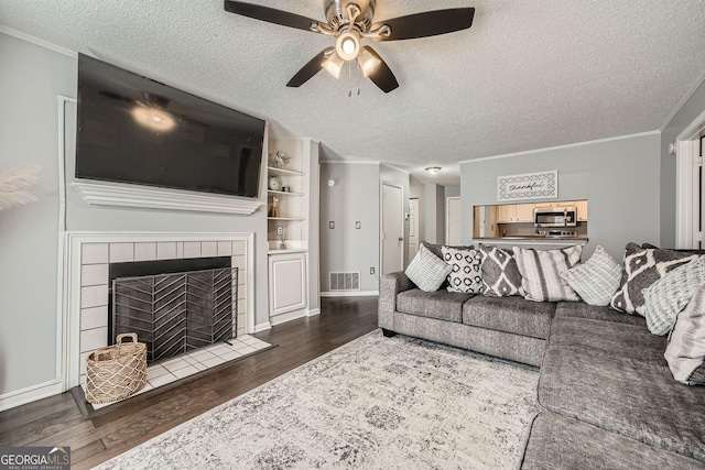 living area with dark wood-style flooring, visible vents, ornamental molding, a textured ceiling, and a tile fireplace