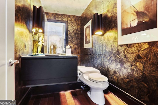 half bathroom featuring wallpapered walls, wood finished floors, toilet, and vanity