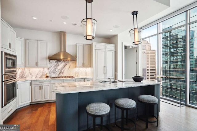 kitchen with a sink, backsplash, floor to ceiling windows, stainless steel appliances, and wall chimney exhaust hood