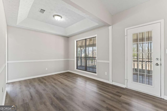 spare room featuring dark wood-type flooring, a raised ceiling, visible vents, and baseboards