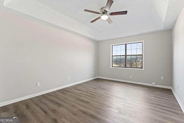 empty room featuring a ceiling fan, baseboards, a tray ceiling, and dark wood-type flooring