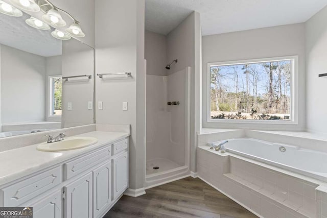 bathroom with wood finished floors, a textured ceiling, a shower stall, vanity, and a bath