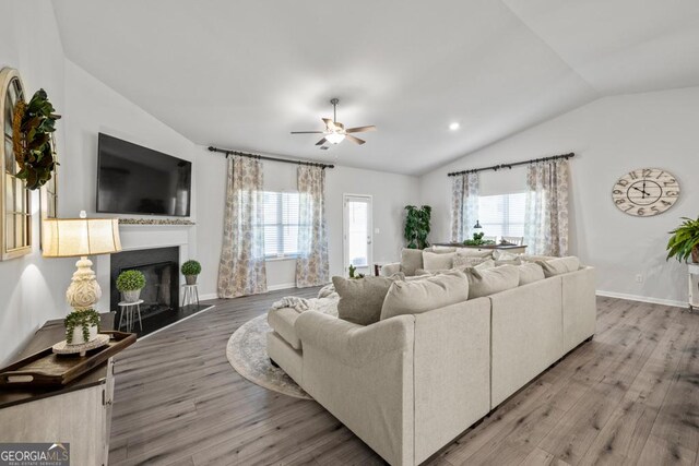 living room with baseboards, ceiling fan, vaulted ceiling, light wood-type flooring, and a fireplace