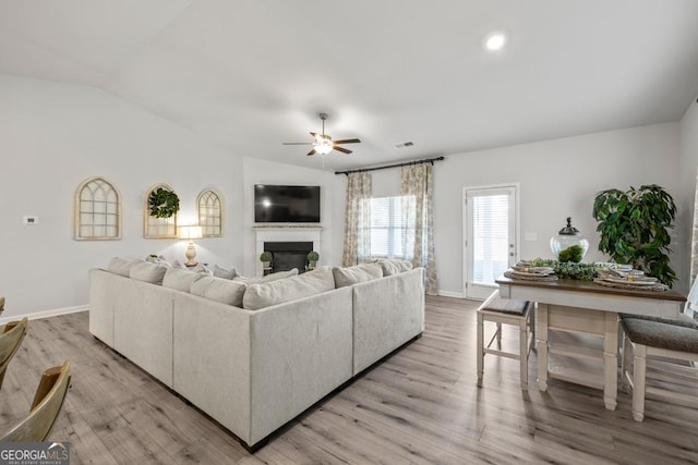 living room with ceiling fan, light wood-type flooring, a glass covered fireplace, and lofted ceiling